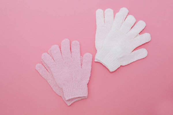Woman exfoliating massage glove for shower on pink background.