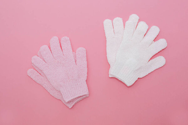 Woman exfoliating massage glove for shower on pink background.