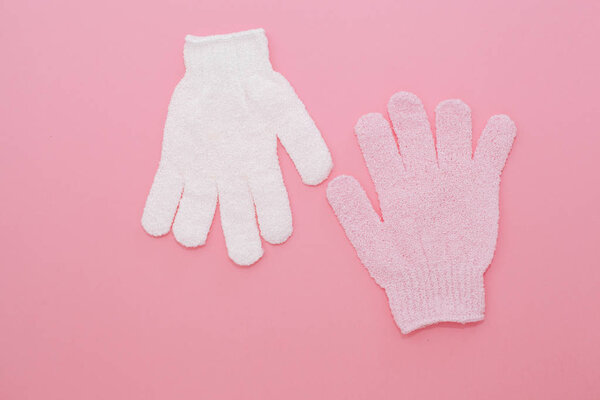 Woman exfoliating massage glove for shower on pink background.