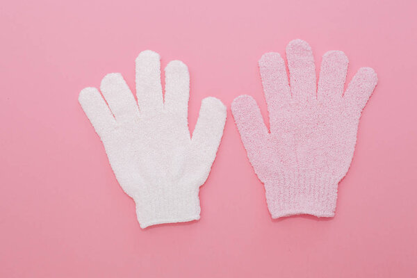 Woman exfoliating massage glove for shower on pink background.