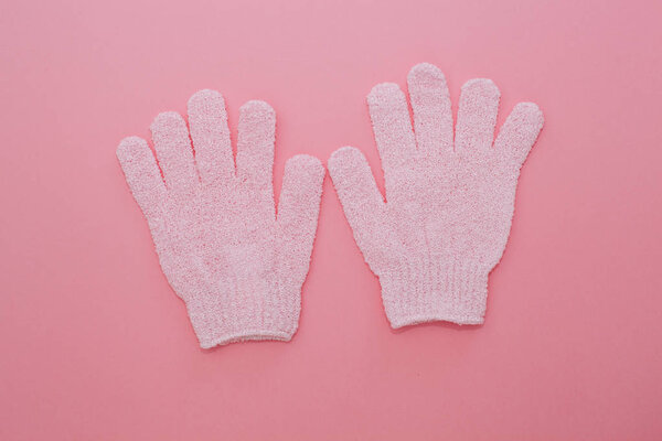 Woman exfoliating massage glove for shower on pink background.