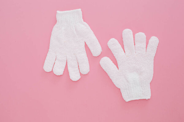 Woman exfoliating massage glove for shower on pink background.