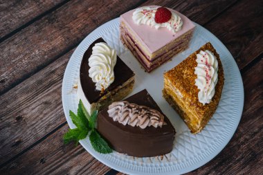 Ahşap arka planda çeşitli kek koleksiyonu. Kremayla dilimlenmiş çeşitli parçalar. Farklı tatlılar içeren tabaklar. Bir sürü lezzetli tatlı dilimi. şekerleme menüsü konsepti