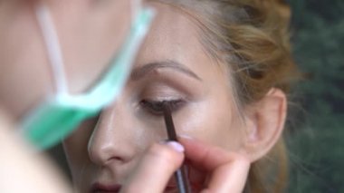 Makyaj yapma süreci. Makyöz yüzüne fırçayla sürmüş. Güzellik salonundaki genç kızıl kadının portresi. Fırçayla makyaj ustasının eli mükemmel cilt ve göz farı yapar. 4k video