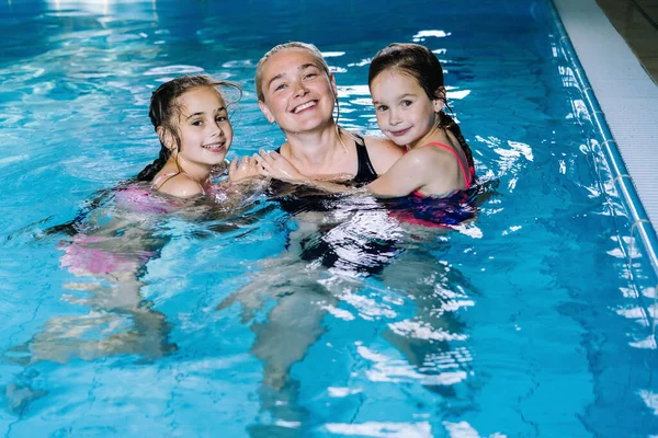 Madre con due figlie che si divertono nella piscina coperta. La ragazza sta riposando al parco acquatico. Scuola di nuoto per bambini piccoli. Concetto amichevole vacanza estiva sportiva familiare. Focus selettivo. — Foto Stock