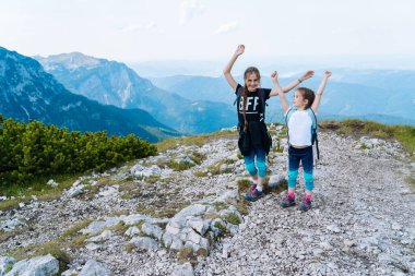 Çocuklar güzel bir yaz günü Alp dağlarında yürüyüş yapıyor Avusturya 'da, kayaların üzerinde dinleniyor ve dağ zirvelerinin muhteşem manzarasına hayran kalıyorlar. Aktif aile tatili. Çocuklarla tatil. Açık hava eğlencesi ve sağlıklı aktivite