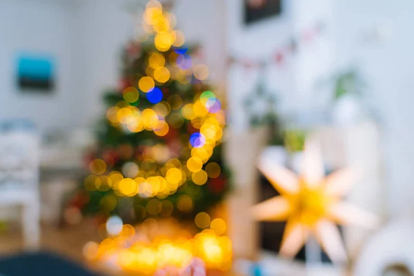 Christmas tree in interior with defocused lights and star. Christmas abstract blur background. Out of focus holiday background with christmas tree. Light bokeh from Xmas tree. Xmas and New Year theme.