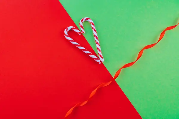 Holiday minimalist decorations. Christmas composition. Present box, Xmas candy canes, red festive decorations on red and green background. Copy space. Xmas and new year holiday concept.