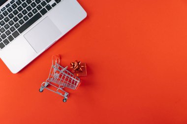 Kredi kartıyla bilgisayardan Noel alışverişi. Yeni yıl dekorasyonları, baston şekerler, alışveriş arabası ve hediye kutusunun üstü kırmızı arka planda yatıyordu. Mutlu Noeller kış tatili satış konsepti.