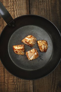 Eski ahşap bir masada, çelik bir tavada kızarmış hindi eti. Koyu arkaplan.