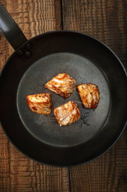 Eski ahşap bir masada, çelik bir tavada kızarmış hindi eti. Koyu arkaplan.