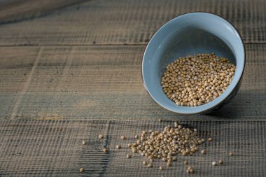 Eski ahşap bir masada seramik bir kasede hardal tohumları. Koyu arkaplan.