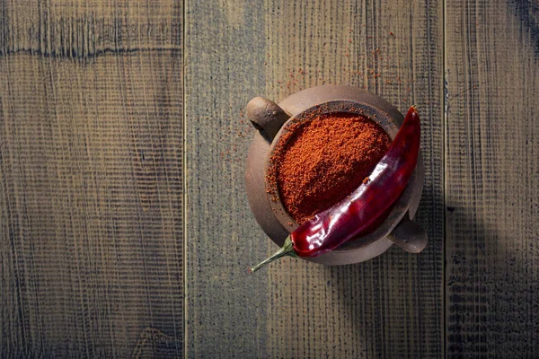 Paprika tozu ve kırmızı biber eski ahşap bir masada seramik bir tencerede. Üst görünüm.