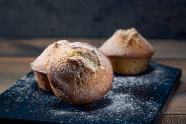 Tahtaya şeker serpiştirilmiş ev yapımı taze kekler. Koyu arkaplan.