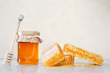 Bal geçmişi. Tarakta tatlı bal, cam kavanoz ve masada bal için bir kaşık. Hafif arkaplan.