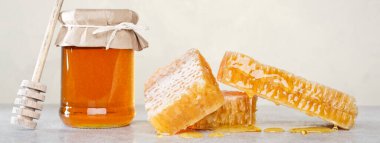 Bal geçmişi. Tarakta tatlı bal, cam kavanoz ve masada bal için bir kaşık. Hafif arkaplan.