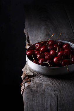 Eski ahşap bir masada metal bir kasede taze, tatlı bir kiraz. Siyah arkaplan.
