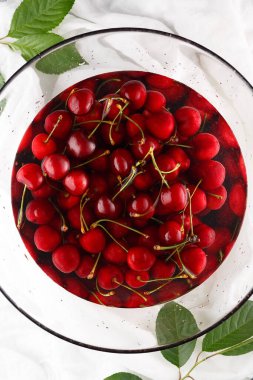 Temiz suyla dolu büyük bir cam kasede taze taze kiraz, yakın plan. Üst görünüm.