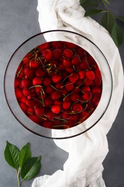Temiz suyla dolu büyük bir cam kasede taze taze kiraz, yakın plan. Üst görünüm.