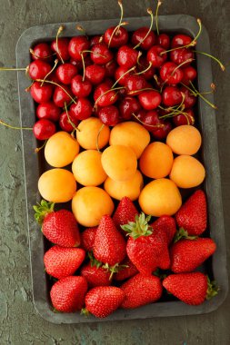 Demir bir kasede olgun taze kayısı, kiraz ve çilek. Üst görünüm,  