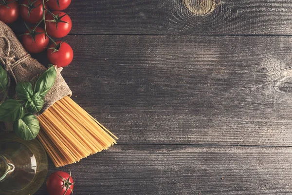 Spagetti, domates, zeytinyağı, eski ahşap bir masada taze fesleğen otu. Mesajın için yer aç. Üst görünüm.