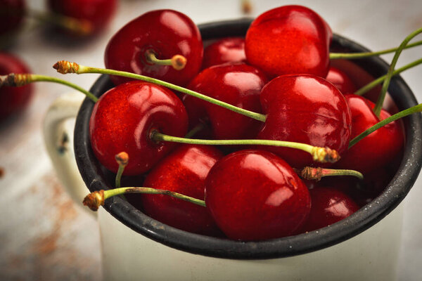 Ripe sweet cherry in an iron cup and scattered on a wooden table