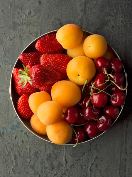 Demir bir kasede olgun taze kayısı, kiraz ve çilek. Üst görünüm,  