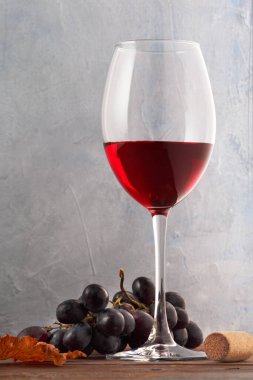 Ahşap bir masada üzüm ve mantarlı bir kadeh kırmızı şarap. Yakın plan.