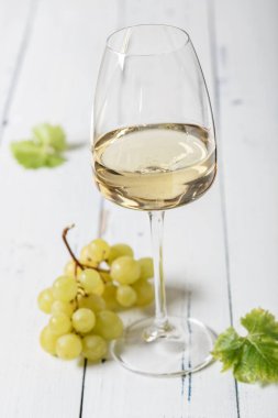 Bardakta beyaz şarap ve eski ahşap bir masada bir demet üzüm.