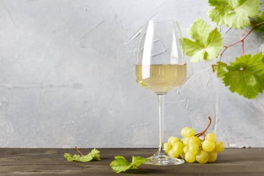 Bardakta beyaz şarap ve eski ahşap bir masada bir demet üzüm.