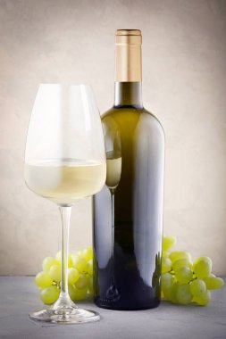 Masada bir şişe beyaz şarap ve bir demet üzüm var..