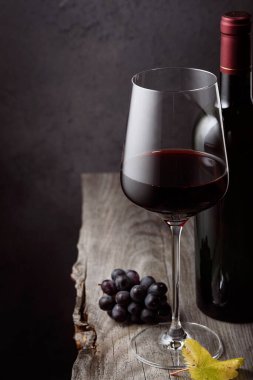 Bir kadeh kırmızı şarap. Üzümlü ve eski ahşap bir masada bir şişe.