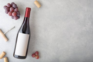 Etiketli bir şişe kırmızı şarap, kırmızı üzüm, mantar ve şişe açacağı. Üst görünüm.