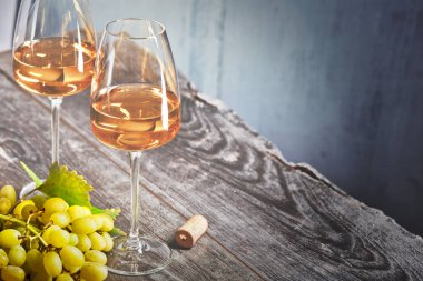 Eski ahşap bir masada iki bardak şarap mantarı ve bir demet üzüm.