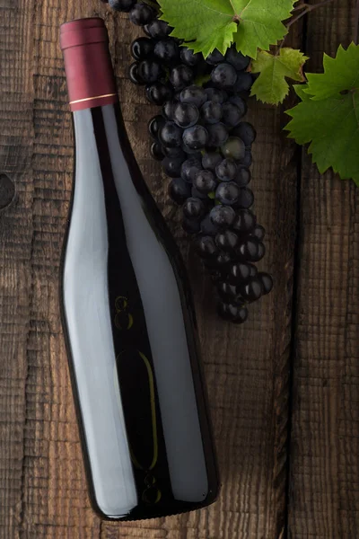 Eski ahşap bir masada bir şişe kırmızı şarap, taze üzüm ve üzüm yeşili yapraklar. Karanlık arka plan. Üst görünüm.