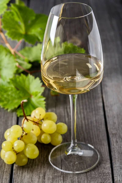 Bardakta beyaz şarap ve eski ahşap bir masada bir demet üzüm.