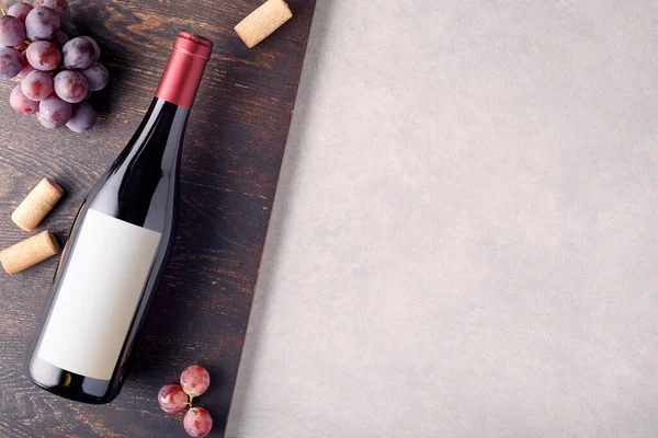 Etiketli bir şişe kırmızı şarap, kırmızı üzüm, mantar ve şişe açacağı. Üst görünüm.
