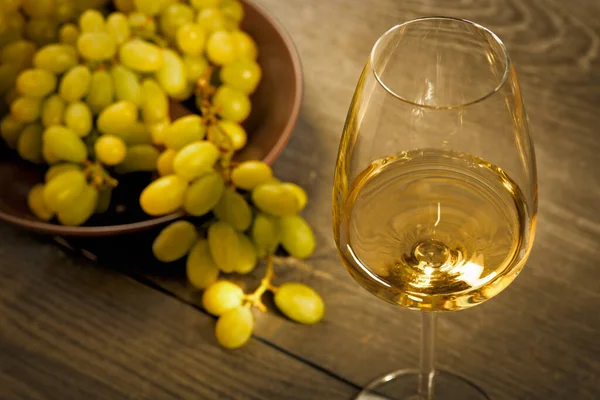 Bir bardak beyaz şarap ve ahşap zemin üzerinde yeşil üzümler.