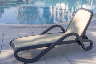 Mavi bir su havuzunun yanında bir iskemle. Sıcak, güneşli bir gün. Yaz tatili.