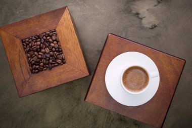 Beyaz fincanda kahve ve masada kahve çekirdekleri. Üst Manzara. Koyu arkaplan.