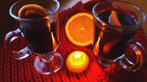 Mulled wine in glass mugs, burning candle on a dark red background. Red Hot wine