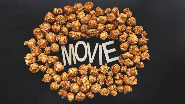 Golden caramel popcorn closeup. Background of popcorn. Wooden letters Movie