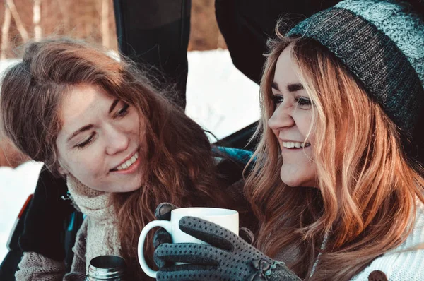 Amigos felizes na floresta de inverno. Duas meninas sentam-se no porta-malas do carro bebendo café — Fotografia de Stock