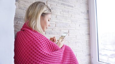 Güzel kız elinde smartphone ile pencere eşiğinde oturuyor.