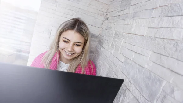 Hermosa mujer joven con un ordenador portátil y cuadros calientes sobre un fondo de ladrillo blanco — Foto de Stock