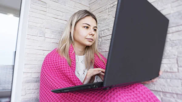 Hermosa mujer joven con un ordenador portátil y cuadros calientes sobre un fondo de ladrillo blanco — Foto de Stock