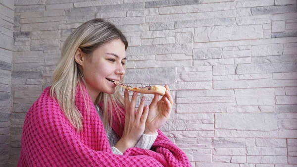 Mulher bonita com xadrez rosa segura uma fatia de pizza na mão e come — Fotografia de Stock