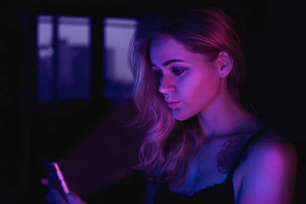 Дівчина використовує мобільний телефон вночі з неоновим світлом — стокове фото