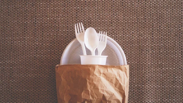 Białe naczynia plastikowe w pakiecie papieru na beżowym tle — Zdjęcie stockowe