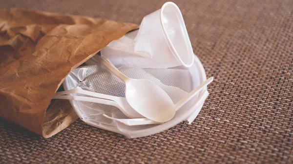 Білий збитий пластиковий посуд у паперовій упаковці на бежевому фоні — стокове фото